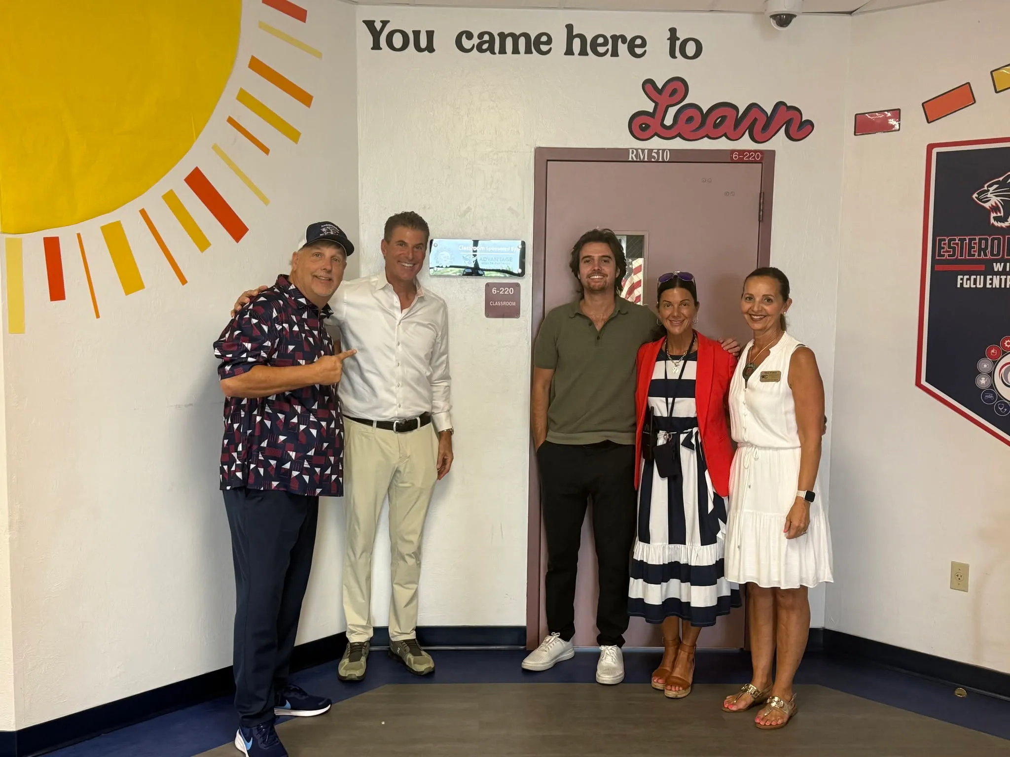 Advantage Wealth Partners team members standing outside the classroom Estero High School dedicated to the firm, below a painted mural that reads You came here to Learn
